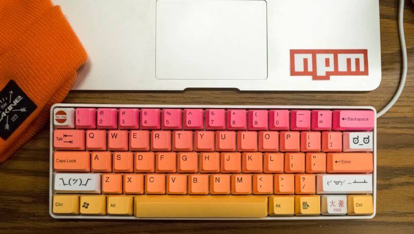 A laptop with npm sticker and an orange keyboard in front of it