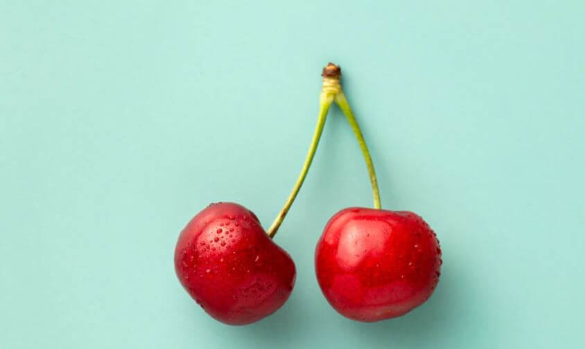 Two cherries on a light teal background